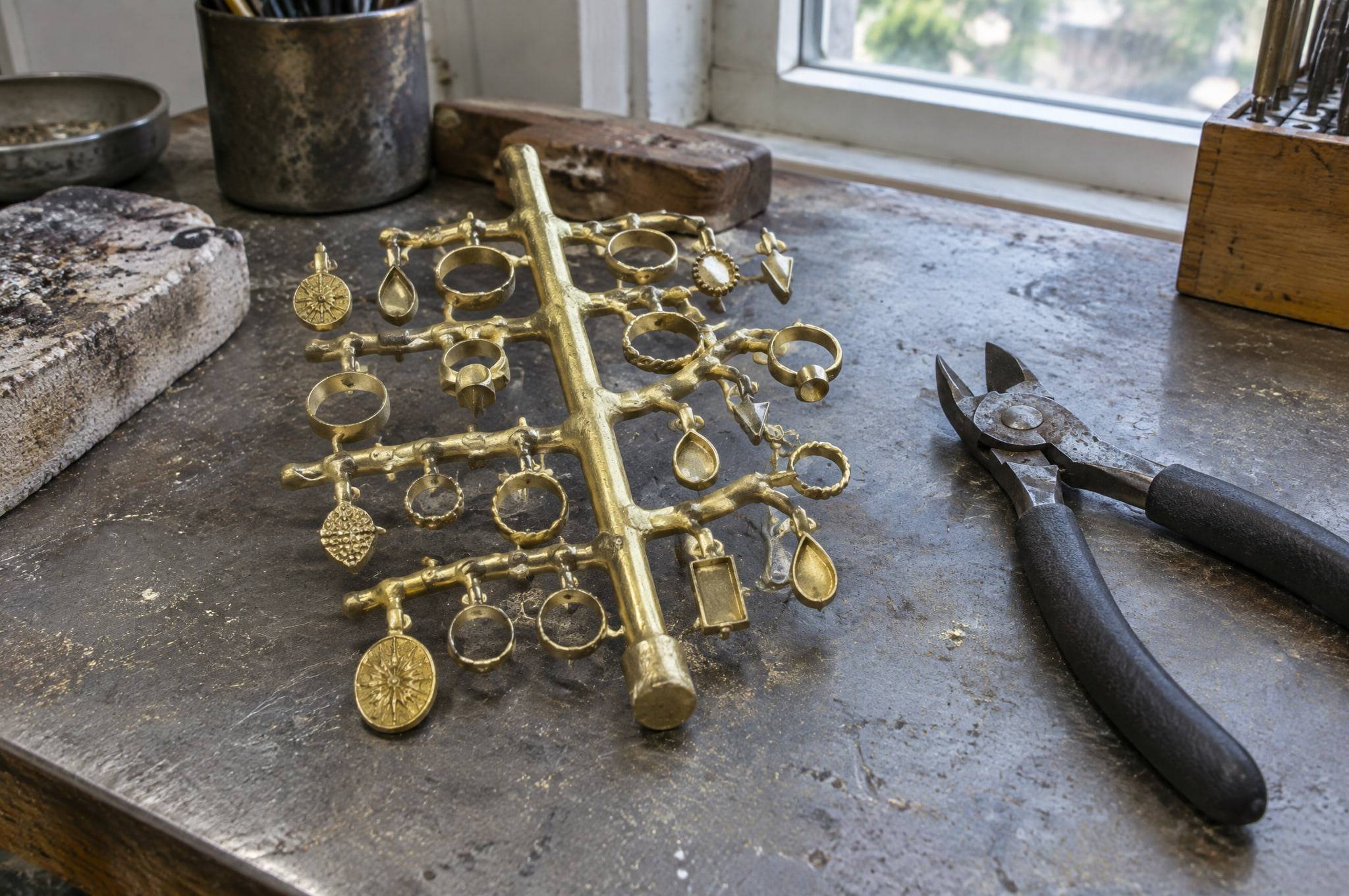 A freshly cast brass casting tree with rings and pendants still attached to the sprue, on a workshop bench.
