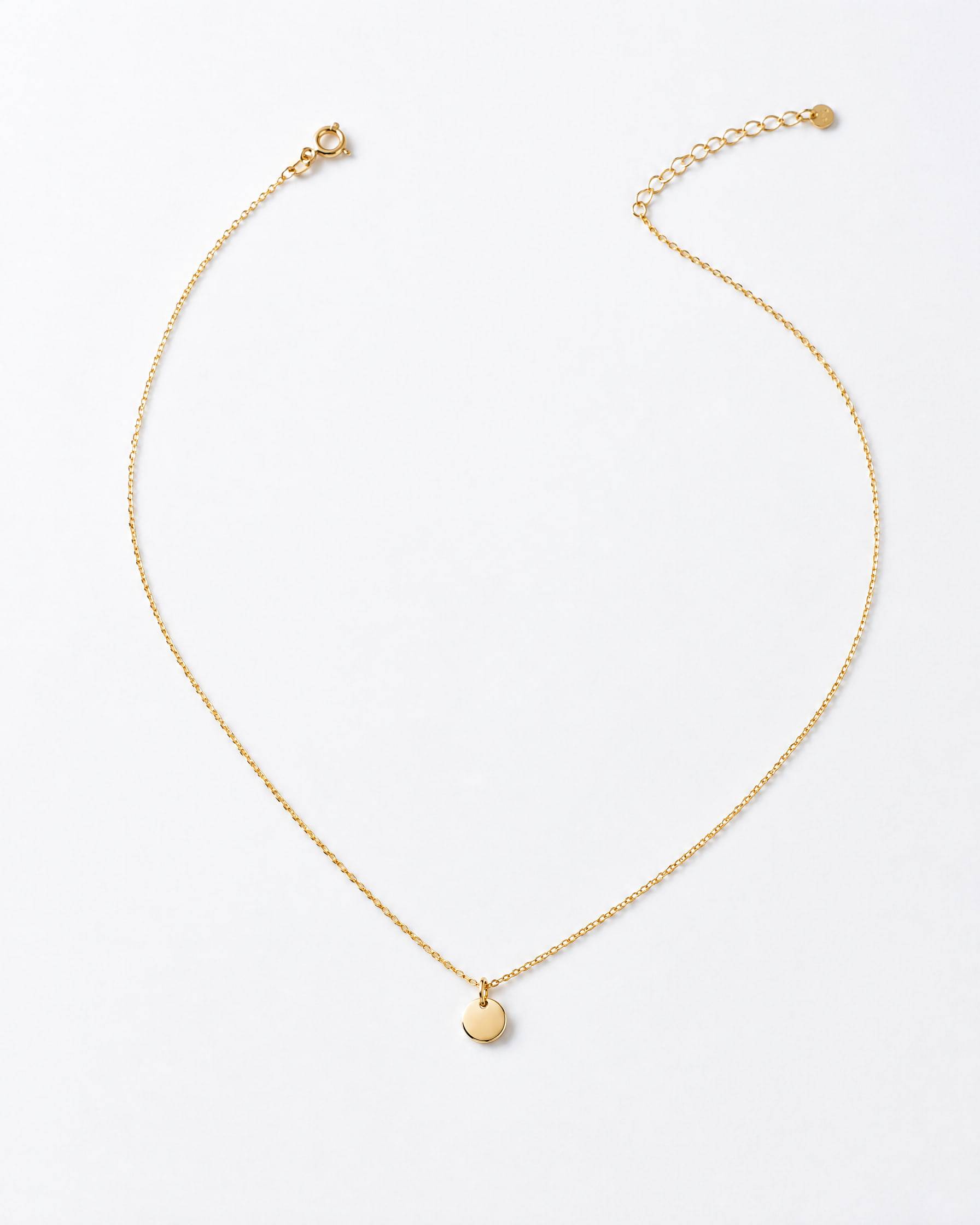 A very fine gold-plated brass chain necklace with a small polished disc pendant, laid on white paper.