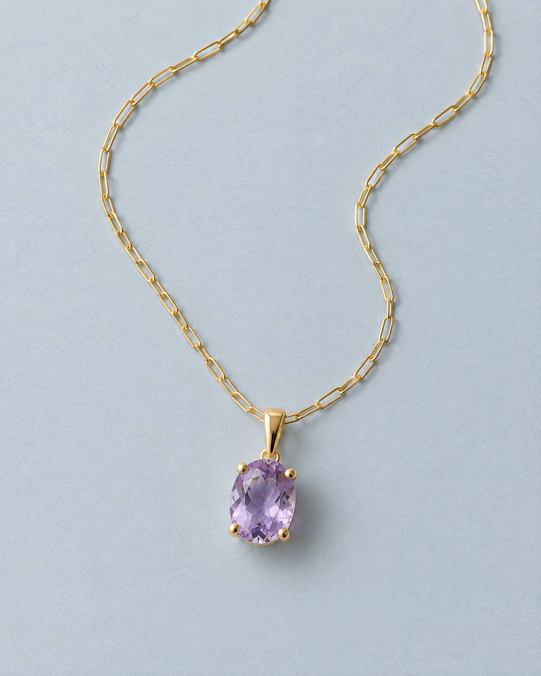 A gold-plated brass pendant with a faceted amethyst in a four-claw setting, on a fine paperclip chain.