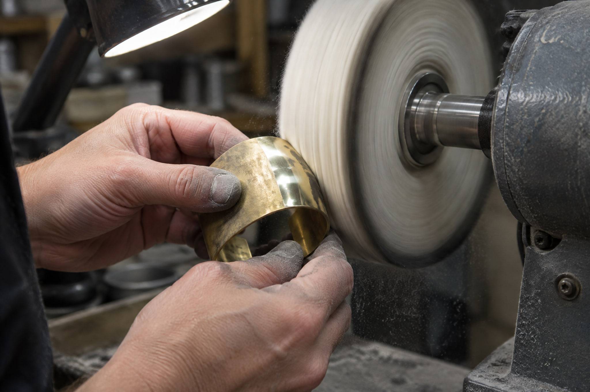 Hands polishing a raw brass cuff against a spinning cotton buffing wheel.