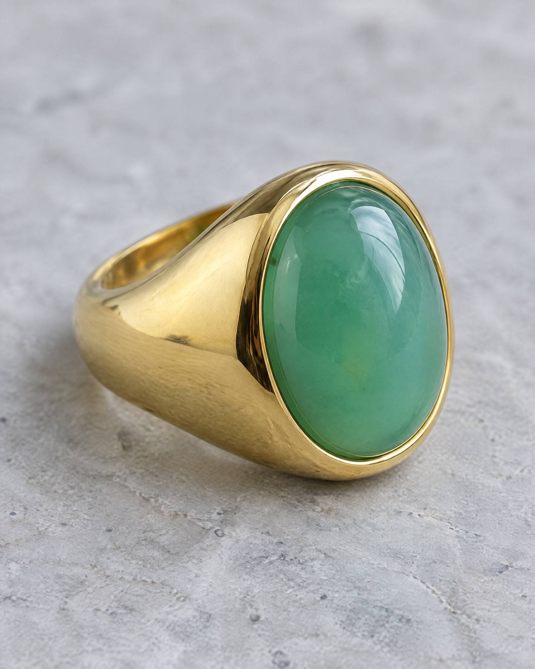A chunky gold-plated brass dome ring set with a large oval green chrysoprase cabochon, on grey stone.