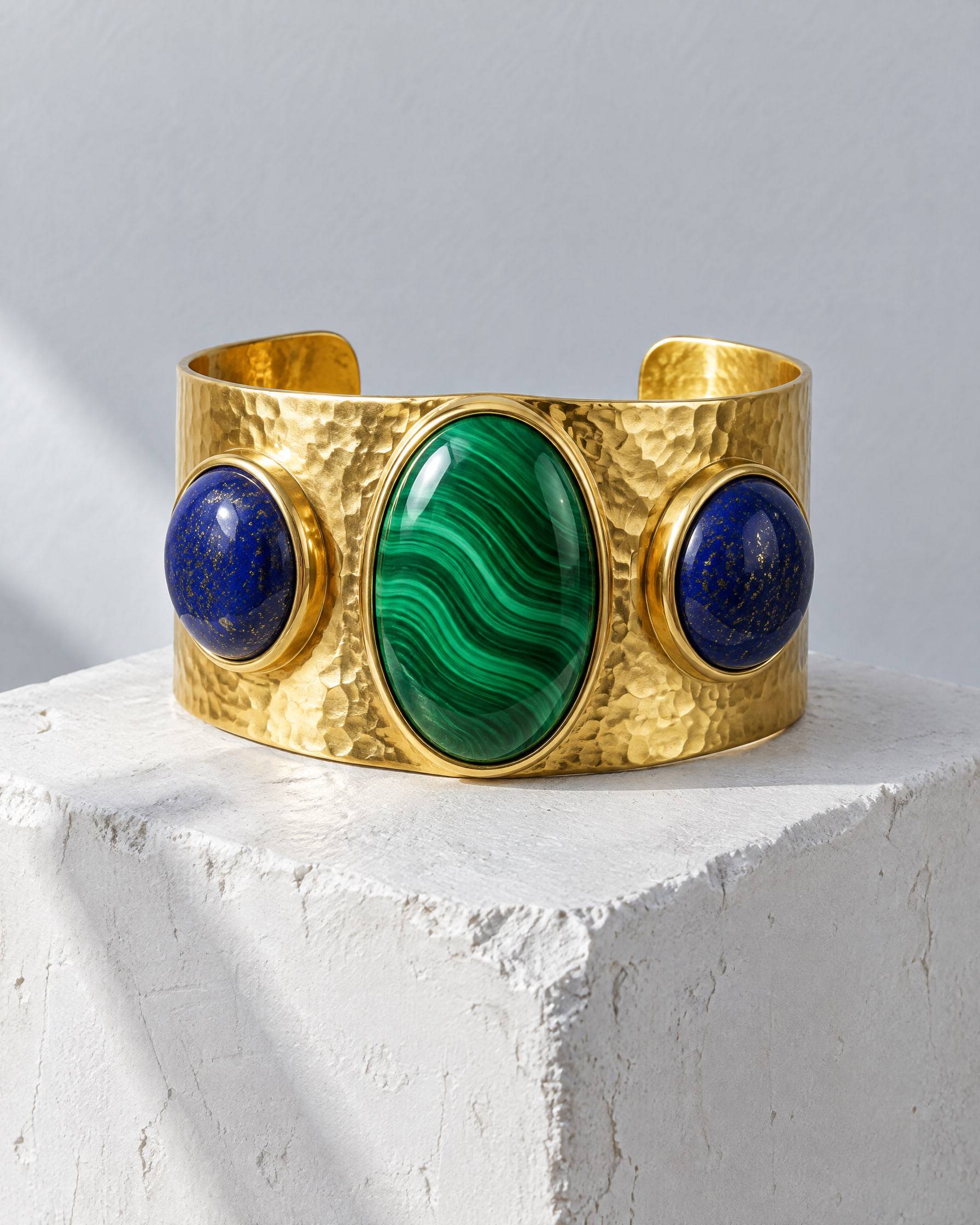 A wide hammered gold-plated brass cuff set with a banded malachite cabochon between two lapis lazuli cabochons.